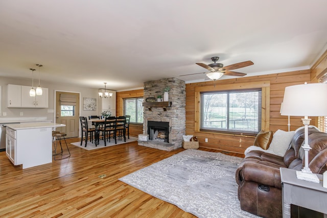 living room featuring ceiling fan with notable chandelier, light hardwood / wood-style floors, a wealth of natural light, and a stone fireplace