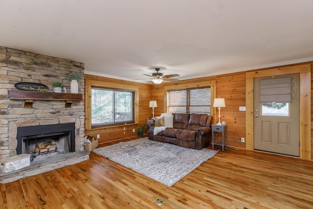 living room with a fireplace, ceiling fan, light hardwood / wood-style floors, and wood walls