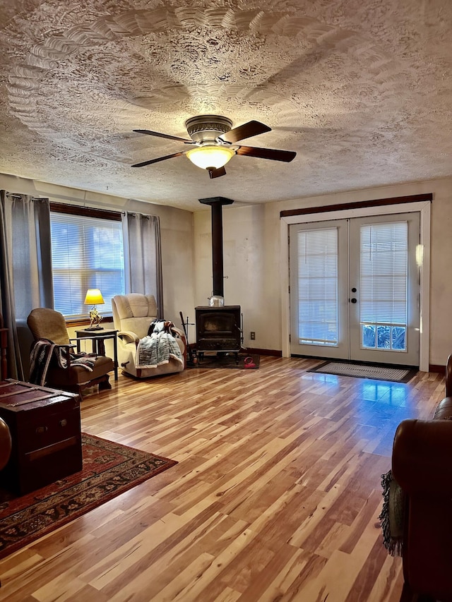 living room featuring french doors, a textured ceiling, ceiling fan, wood-type flooring, and a wood stove