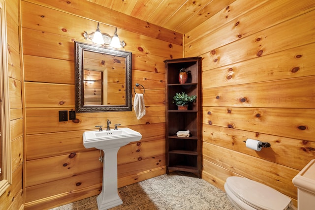 bathroom with toilet, wooden ceiling, sink, and wooden walls