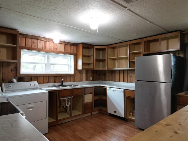 kitchen featuring stainless steel refrigerator, dishwasher, sink, wood walls, and light hardwood / wood-style floors