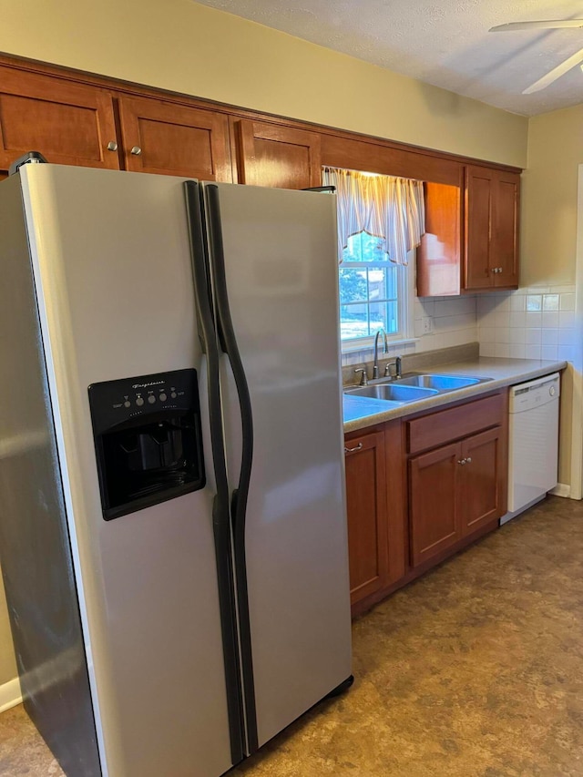 kitchen featuring decorative backsplash, stainless steel refrigerator with ice dispenser, white dishwasher, ceiling fan, and sink