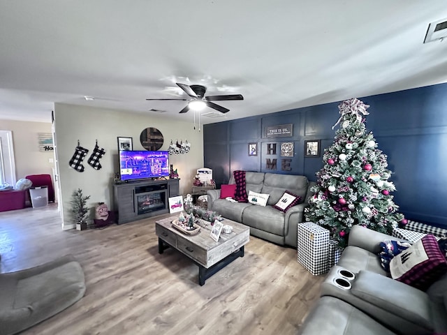 living room with a fireplace, light wood-type flooring, and ceiling fan