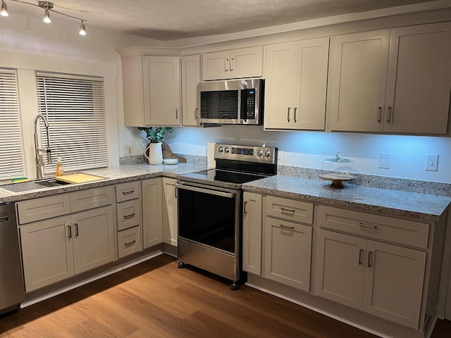 kitchen with appliances with stainless steel finishes, a textured ceiling, light hardwood / wood-style flooring, and sink