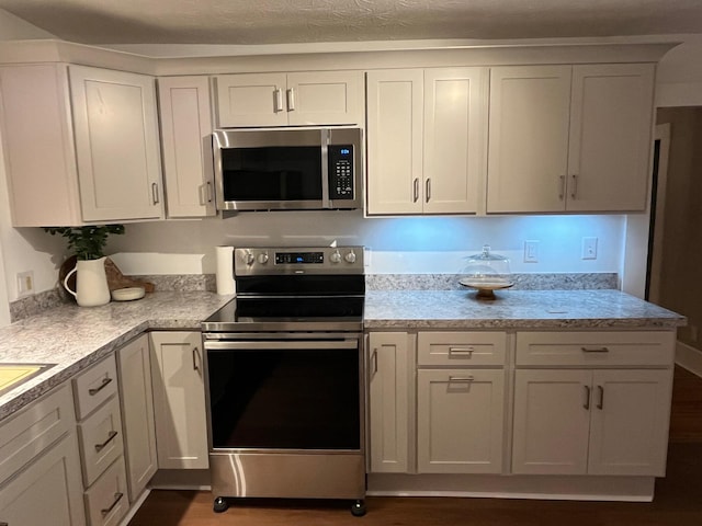 kitchen featuring dark hardwood / wood-style flooring, white cabinets, stainless steel appliances, and a textured ceiling