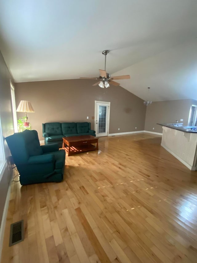 living room featuring ceiling fan with notable chandelier, vaulted ceiling, and light hardwood / wood-style flooring