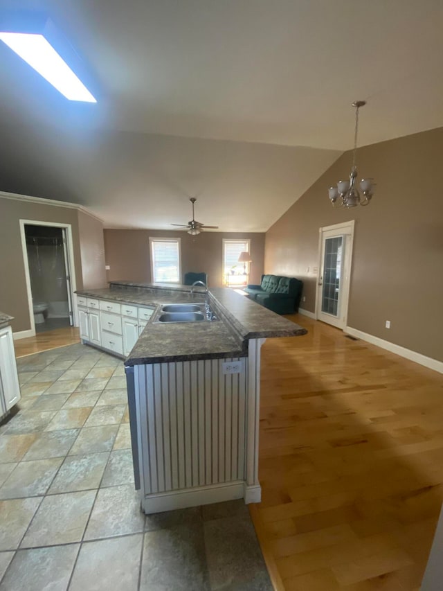 kitchen featuring sink, decorative light fixtures, vaulted ceiling with skylight, white cabinets, and light wood-type flooring