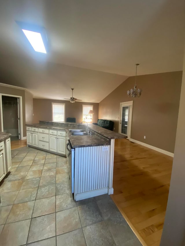 kitchen with lofted ceiling with skylight, sink, white cabinets, and hanging light fixtures