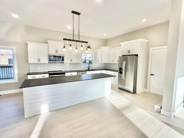 kitchen with a sink, stainless steel appliances, dark countertops, tasteful backsplash, and a center island