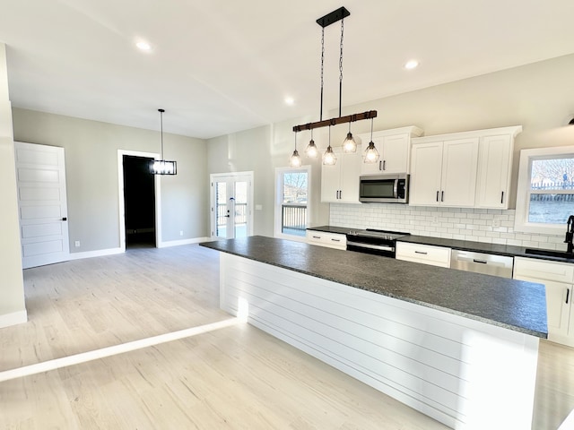 kitchen featuring dark countertops, tasteful backsplash, light wood-style flooring, stainless steel appliances, and a sink