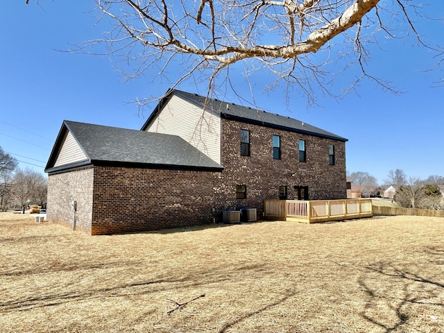 back of property with a deck, central AC unit, brick siding, and roof with shingles