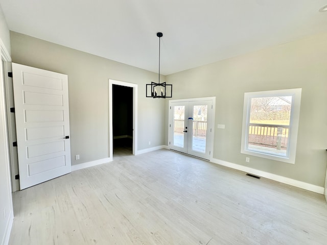 empty room with visible vents, a notable chandelier, french doors, light wood finished floors, and baseboards