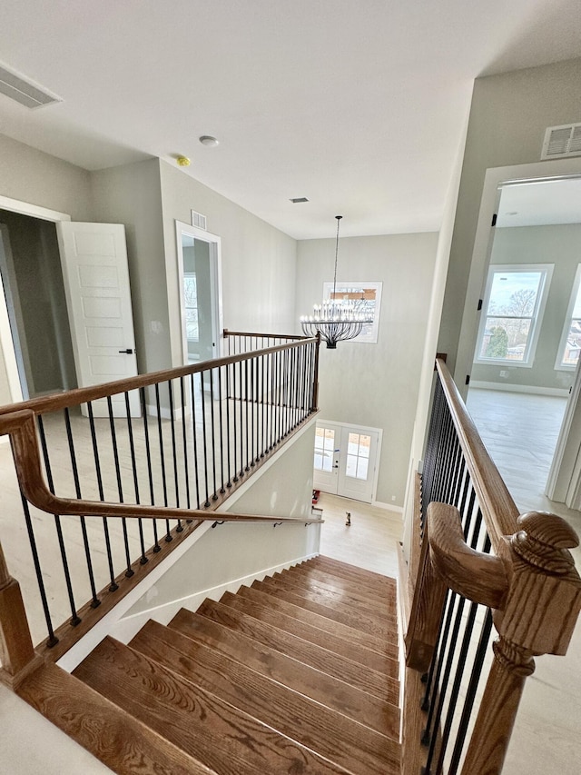 stairway featuring visible vents, baseboards, an inviting chandelier, and wood finished floors