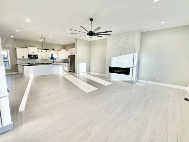 unfurnished living room featuring light wood-style floors, baseboards, a large fireplace, and ceiling fan