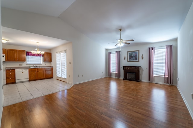 unfurnished living room with vaulted ceiling, plenty of natural light, ceiling fan with notable chandelier, and light hardwood / wood-style flooring