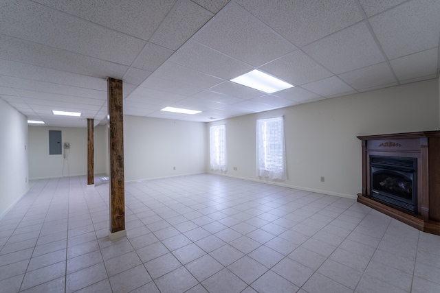 basement featuring a paneled ceiling, light tile patterned floors, and electric panel