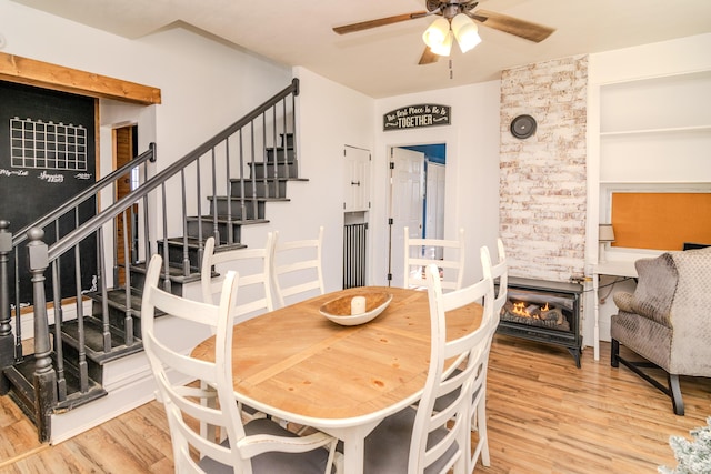 dining space featuring wood-type flooring, a stone fireplace, and ceiling fan