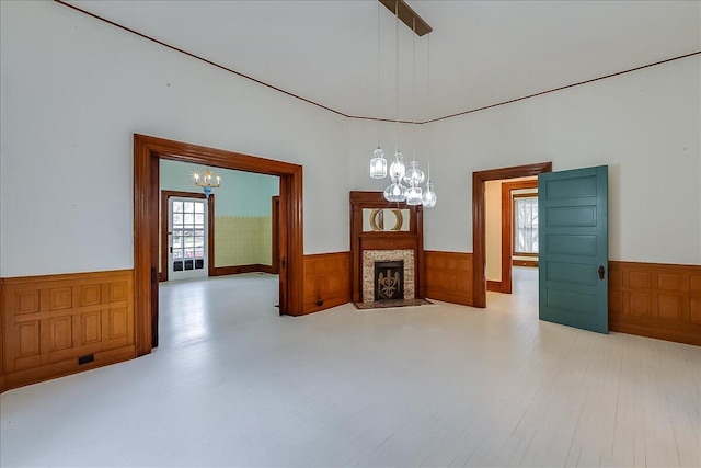 spare room with a chandelier, light hardwood / wood-style flooring, a stone fireplace, and wooden walls