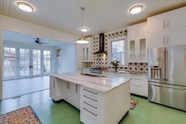 kitchen with wall chimney exhaust hood, stainless steel appliances, pendant lighting, a kitchen island with sink, and white cabinets