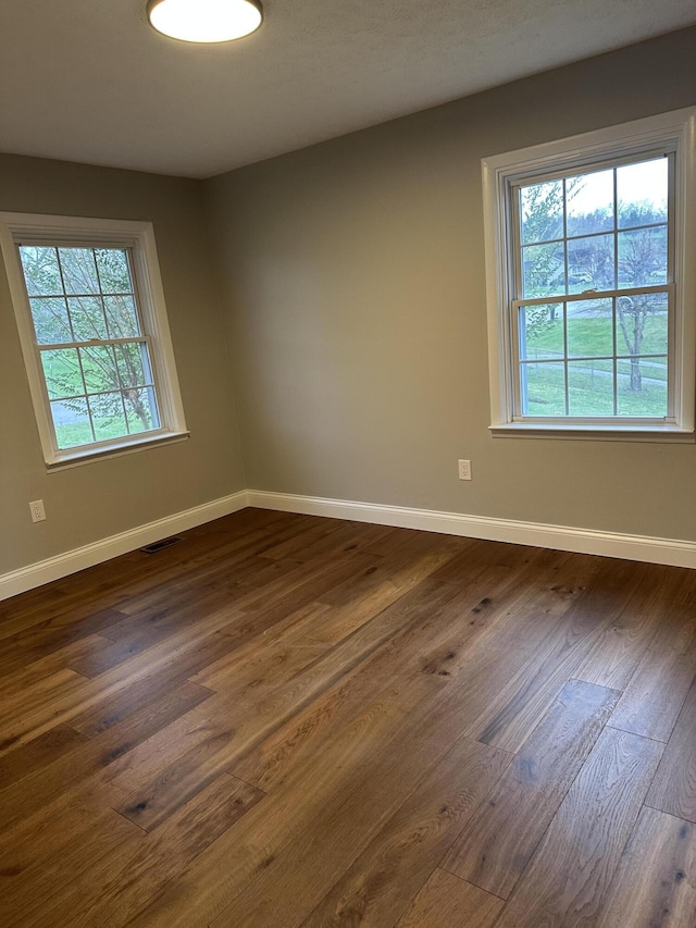 empty room featuring a wealth of natural light, visible vents, dark wood-type flooring, and baseboards