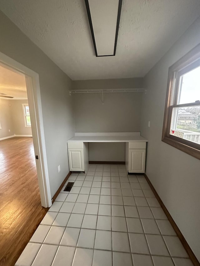 interior space featuring light tile patterned floors, visible vents, baseboards, and a textured ceiling