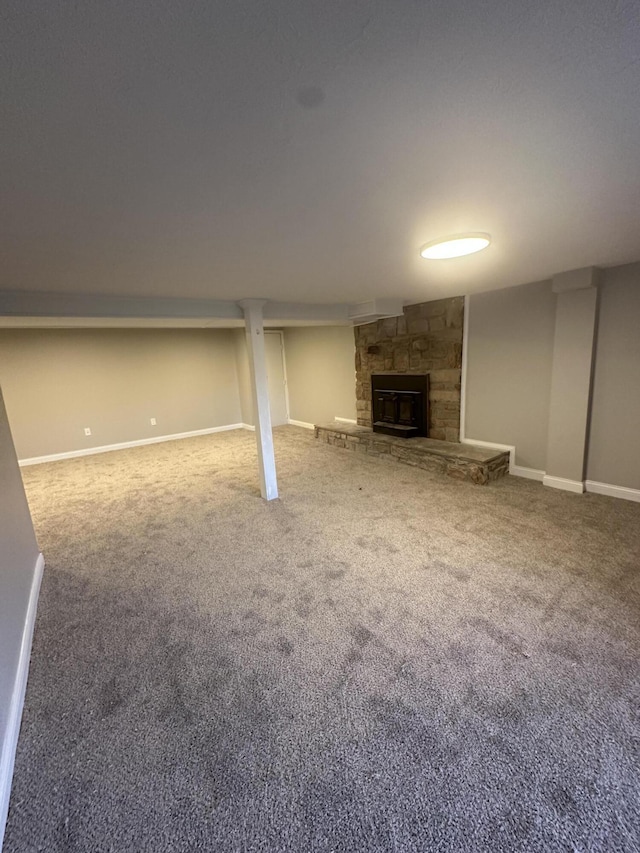 finished below grade area featuring a stone fireplace, baseboards, and carpet floors