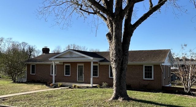 single story home featuring brick siding, covered porch, a chimney, and a front yard