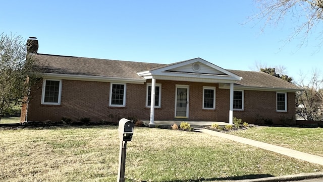 ranch-style house featuring a porch, roof with shingles, a front yard, brick siding, and a chimney