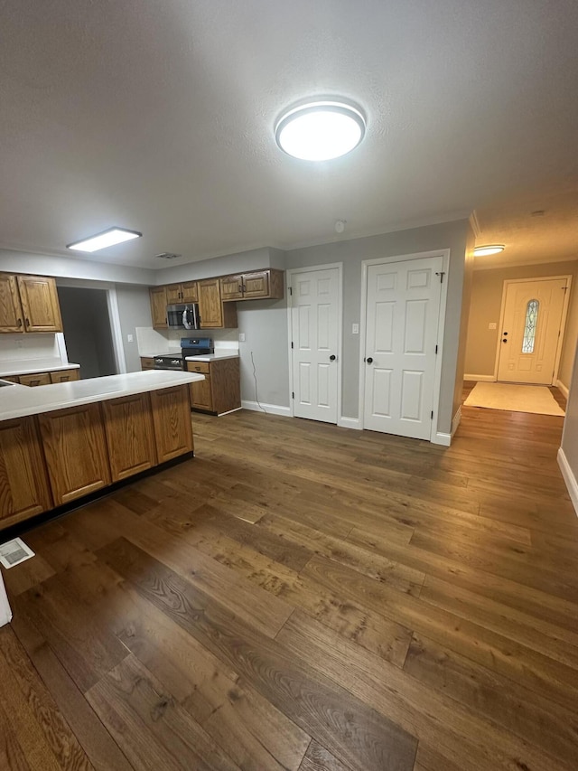 kitchen featuring dark wood finished floors, baseboards, brown cabinets, and appliances with stainless steel finishes