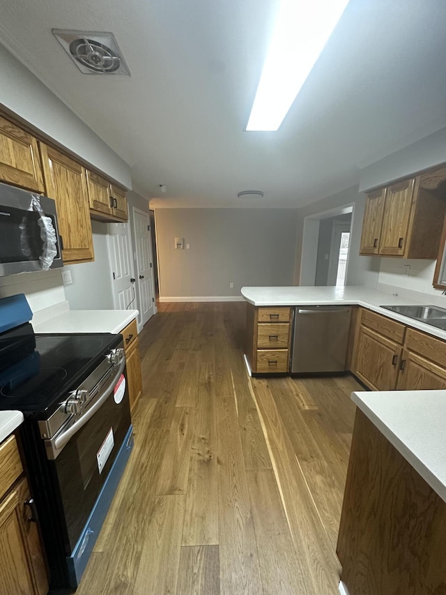 kitchen featuring appliances with stainless steel finishes, wood finished floors, brown cabinetry, and light countertops