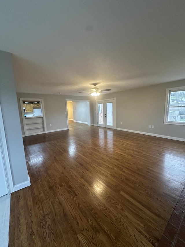 unfurnished living room with dark wood-type flooring, a ceiling fan, and baseboards