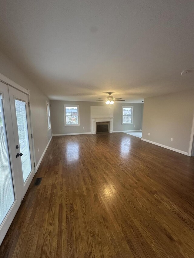 unfurnished living room with visible vents, baseboards, a fireplace, ceiling fan, and dark wood-type flooring