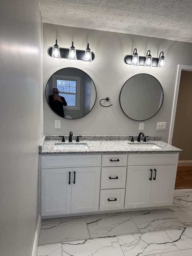 bathroom with a sink, a textured ceiling, marble finish floor, and double vanity