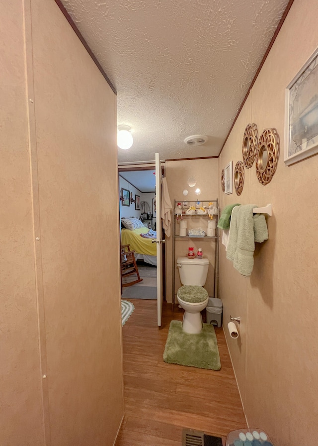 bathroom featuring a textured ceiling, hardwood / wood-style flooring, toilet, and crown molding