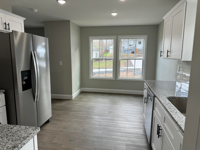 kitchen featuring white cabinets, light hardwood / wood-style floors, light stone countertops, and stainless steel appliances