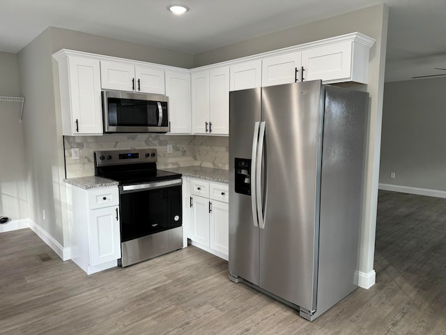 kitchen with white cabinetry, light stone countertops, backsplash, appliances with stainless steel finishes, and light wood-type flooring