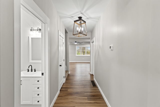 corridor with dark hardwood / wood-style floors, an inviting chandelier, and sink