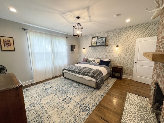 bedroom with dark wood-type flooring, a notable chandelier, and a brick fireplace