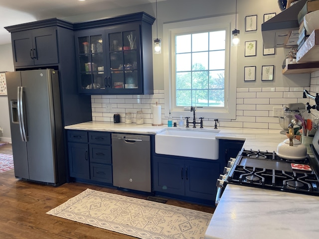 kitchen with stainless steel appliances, sink, blue cabinetry, decorative light fixtures, and dark hardwood / wood-style floors