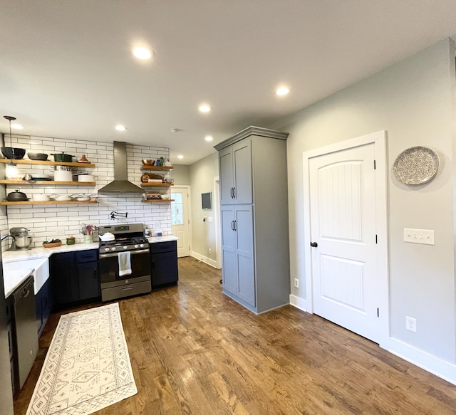 kitchen featuring gray cabinetry, dark wood-type flooring, wall chimney range hood, decorative backsplash, and appliances with stainless steel finishes