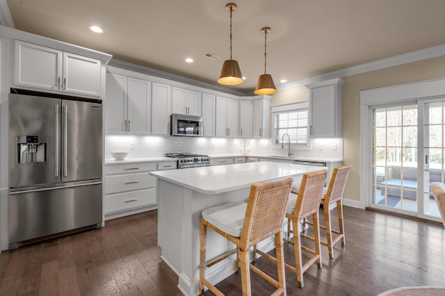 kitchen with sink, white cabinets, pendant lighting, a kitchen island, and appliances with stainless steel finishes