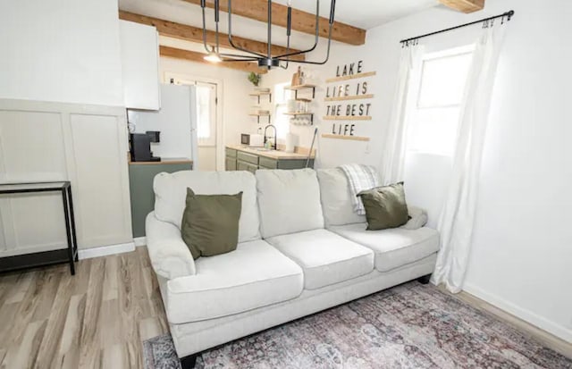 living room featuring beam ceiling, sink, a chandelier, and light wood-type flooring