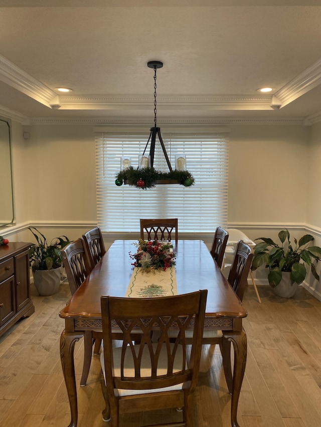 dining area with a tray ceiling, crown molding, and light wood-type flooring