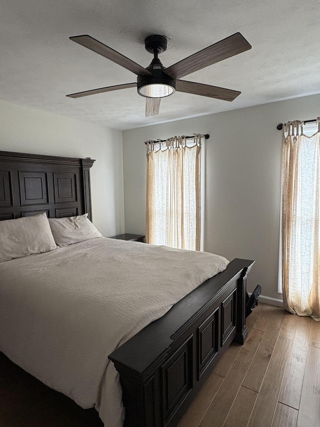 bedroom with ceiling fan, wood-type flooring, and multiple windows