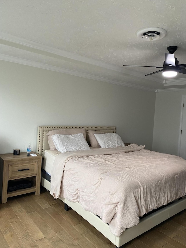 bedroom with ceiling fan, wood-type flooring, a textured ceiling, and ornamental molding