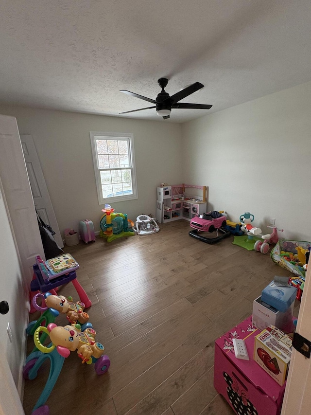 recreation room with hardwood / wood-style floors, ceiling fan, and a textured ceiling