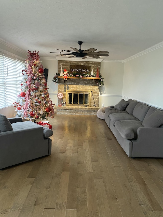 living room featuring hardwood / wood-style floors, ceiling fan, crown molding, and a brick fireplace