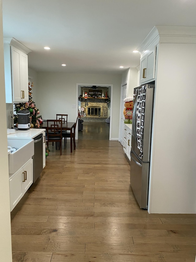 kitchen featuring a stone fireplace, white cabinetry, light hardwood / wood-style flooring, and appliances with stainless steel finishes