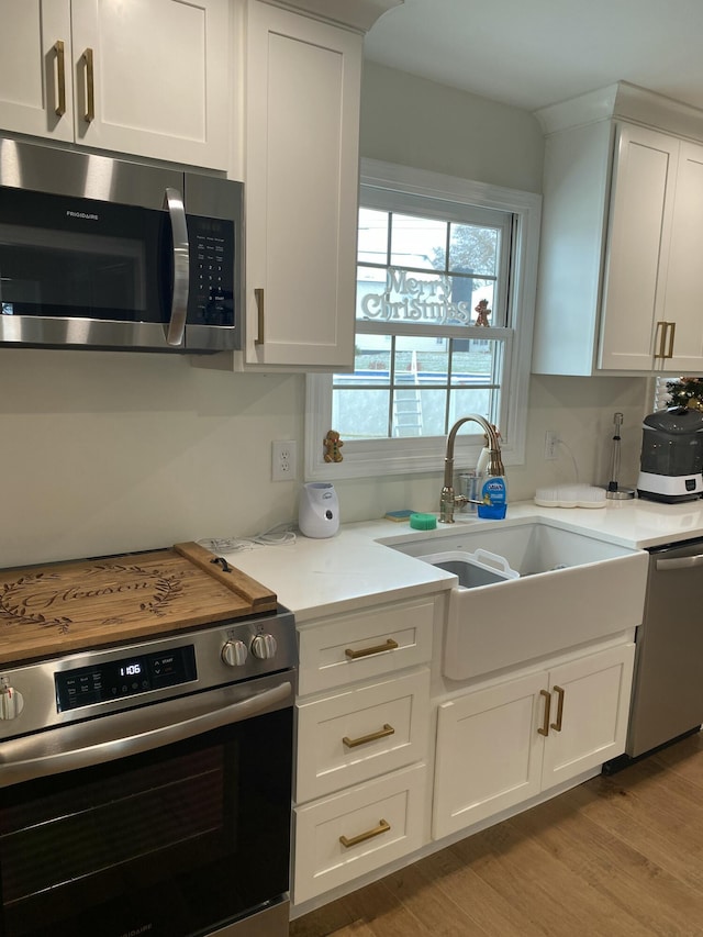 kitchen featuring light stone countertops, stainless steel appliances, sink, white cabinets, and light hardwood / wood-style floors