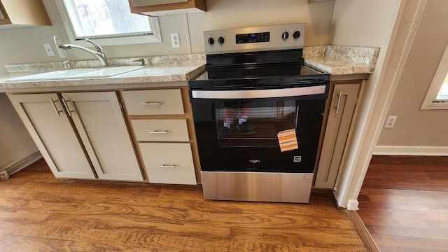 kitchen with light countertops, baseboards, wood finished floors, a sink, and stainless steel electric stove